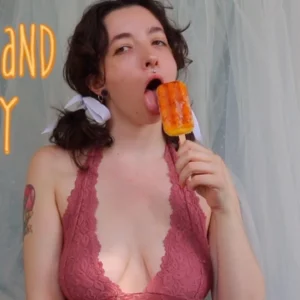 Brunette in pigtails and a pink halter top licking a mango popsicle seductively title "Wet and Sticky" watermark @TheLusciousLibra