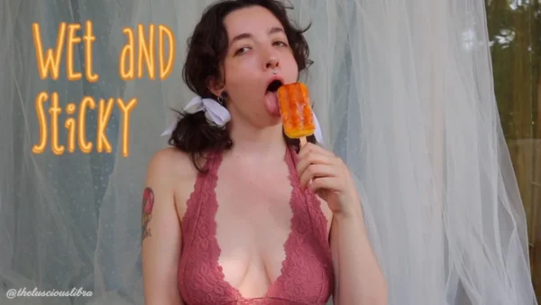 Brunette in pigtails and a pink halter top licking a mango popsicle seductively title "Wet and Sticky" watermark @TheLusciousLibra