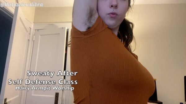 Bodacious brunette wearing tight orange t-shirt showing off her fuzzy armpits. Title reads "Sweaty After Self Defense Class (Hairy Armpit Worship)"
